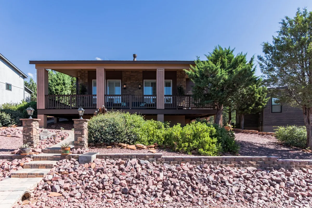 A welcoming front porch with rock landscaping, green shrubs, and a stone pathway creates an inviting transition between indoor and outdoor living. The scene suggests a quiet spot for morning coffee or evening relaxation, with natural elements enhancing the peaceful mood.