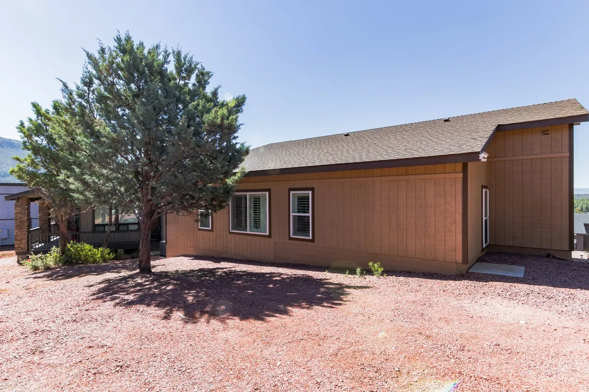 This image features the exterior of the house set beneath a prominent tree, with a clear sky overhead. The landscaping is natural and inviting, suggesting a peaceful, open space ideal for relaxation or walks. There is a sense of connection with nature, and the outdoor area feels accessible for both people and pets.