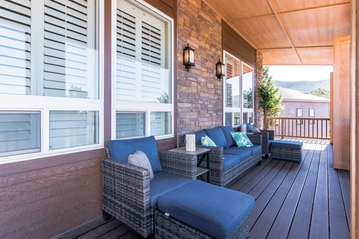 This exterior image captures a comfortable outdoor seating area set atop a deck, featuring decorative pillows, stone wall accents, and stylish lanterns. The arrangement is oriented to take in views of the surrounding trees, with warm, natural light creating an inviting, tranquil atmosphere—perfect for morning coffee, reading, or sunset toasts.
