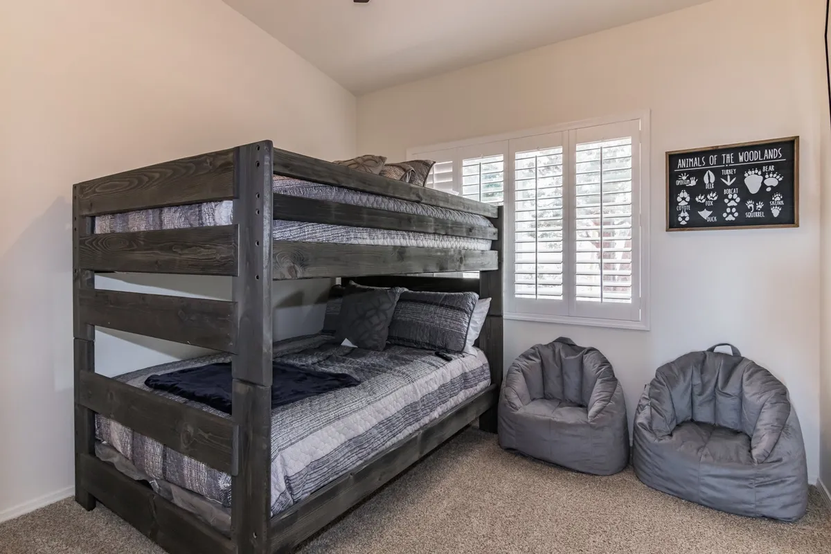 A playful yet cozy bunk room with a double-on-double bunk bed, bean bag chairs, and whimsical animal-themed artwork. The space is designed for comfort and fun, ideal for children or friends sharing the room.