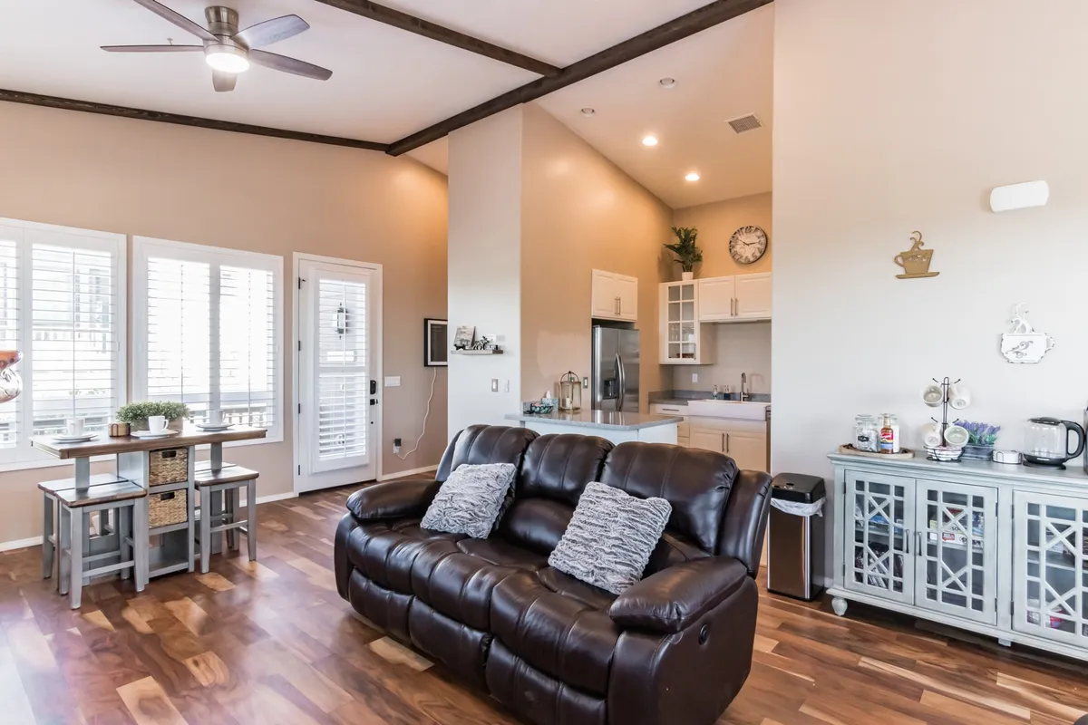 This image captures a seamless open-concept living space featuring a leather sofa, a dining table, and a kitchen area with decorative accents. The room is bathed in natural light, highlighting the flow between lounging, dining, and cooking areas.