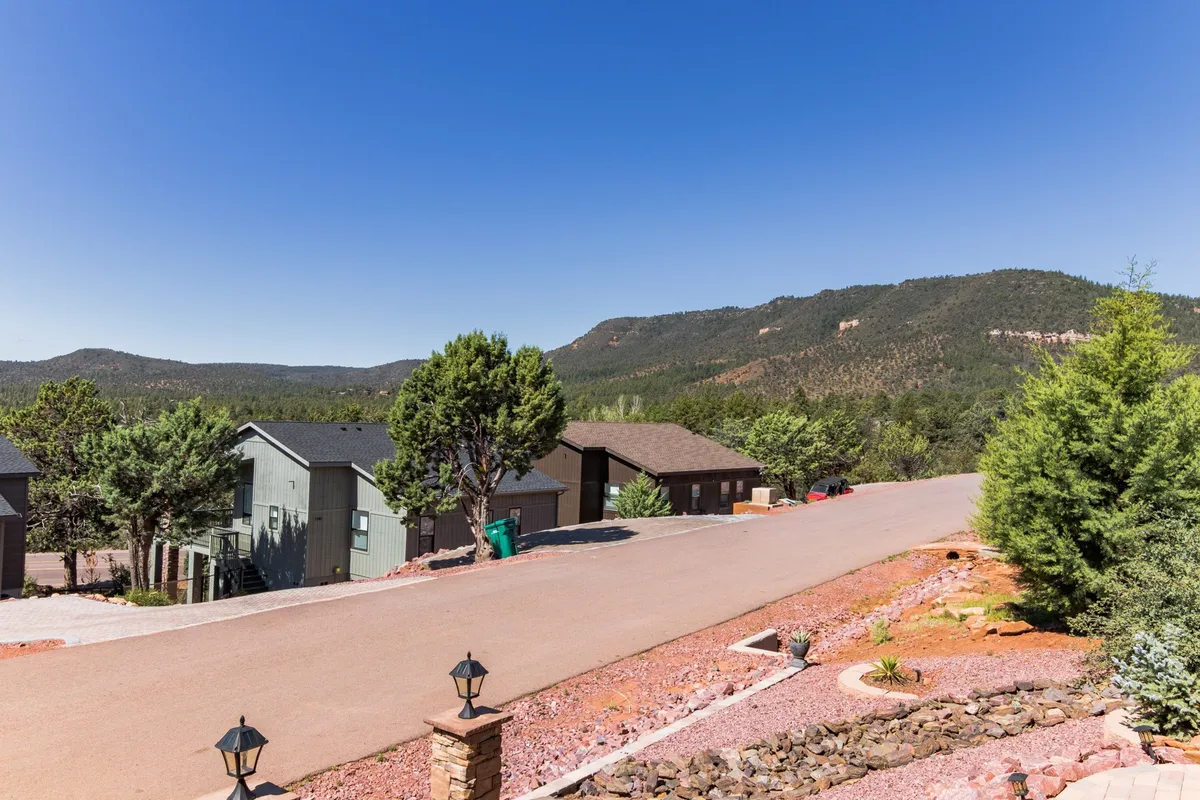 This image presents a sweeping view of a mountain range rising above a line of trees and residential houses, with a paved road winding through the foreground. The tranquil setting evokes the area’s natural beauty and offers a sense of proximity to outdoor adventures like hiking, biking, and nature walks.