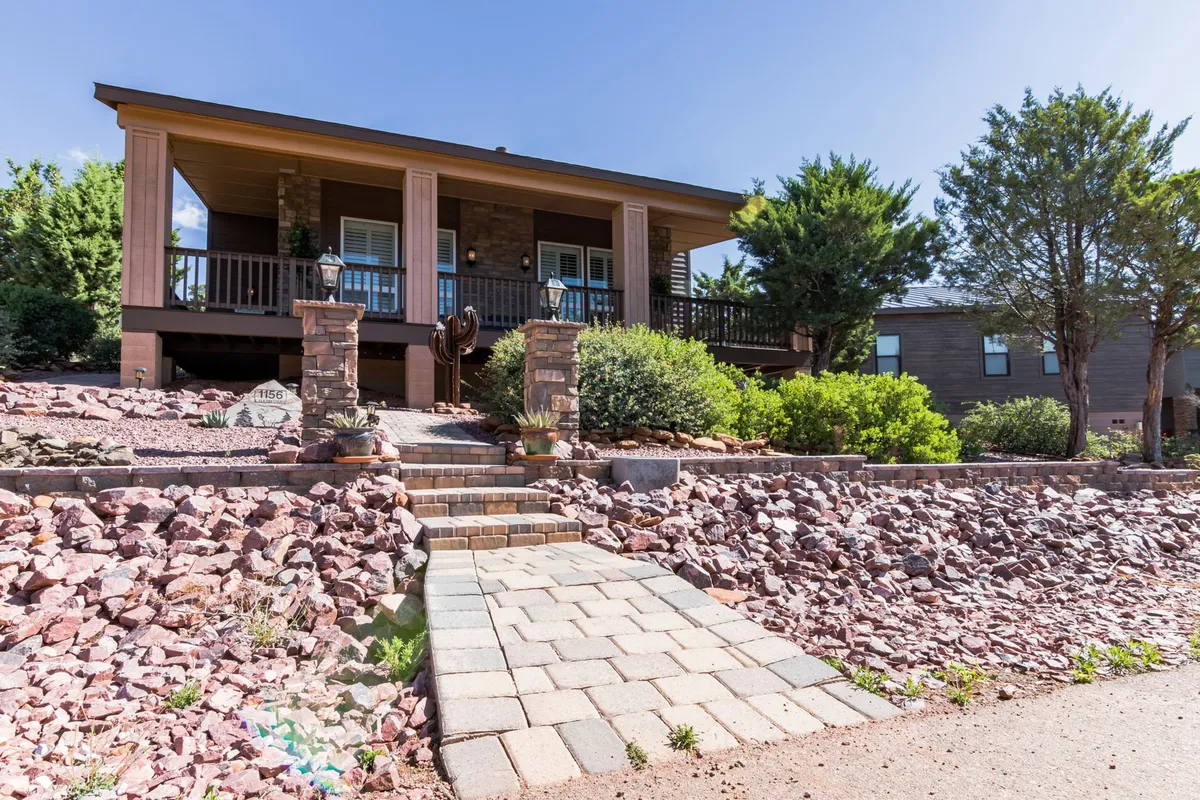 The front porch with stone steps leads up to a cozy seating area, framed by landscaped greenery and blooming flowers. The setting exudes a sense of welcome and offers a peaceful spot to enjoy the outdoors.