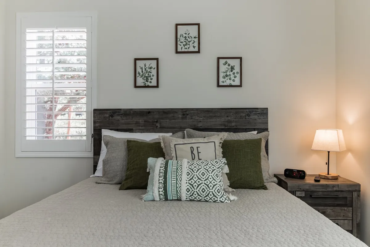 A serene bedroom featuring a comfortable bed adorned with decorative pillows, framed botanical prints above the headboard, and a cozy nightstand with a lamp. Soft, natural light fills the room, creating a peaceful setting ideal for relaxation and deep rest.